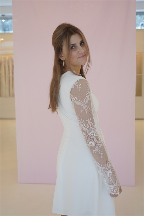 Konfirmationskjole Lea i satin og fine blonder. Kjolen har et asymmetrisk snit med draperinger, lange blondeærmer. Dertil et lækkert fit and flare skørt. Prøv Lea og vores øvrige konfirmationskjoler i vores Butik/Showroom.